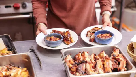 A person holds plates of prepared food in a kitchen.