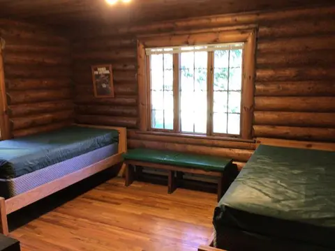 An interior view of a log cabin bedroom with two twin beds and a window.