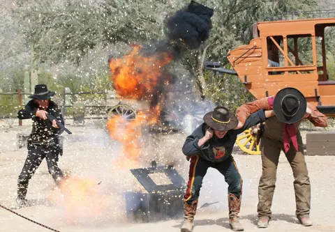 An explosion goes off near men in cowboy costumes in an outdoor setting.