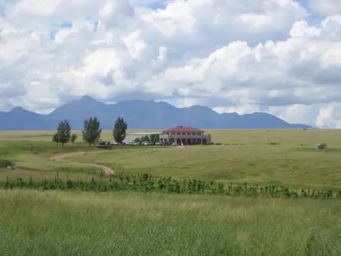 A building sits in a grassy plain with mountains in the background.