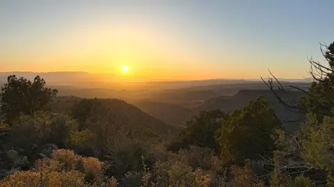 A sunset view over a vast landscape with hills and vegetation.