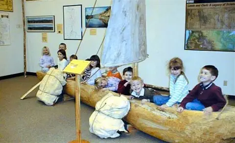 Children sit inside a wooden canoe model in a museum.