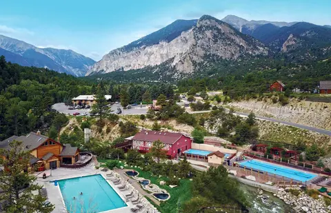 An aerial view shows a resort with multiple swimming pools nestled in a mountainous landscape.