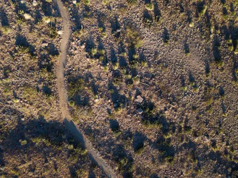 An aerial view of a winding dirt trail through a desert landscape with sparse vegetation.