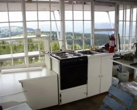 Interior of a lookout tower showing a kitchen counter, stove, and windows overlooking a landscape.