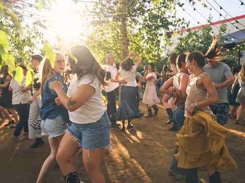 A group of people dancing outdoors in the sunlight.