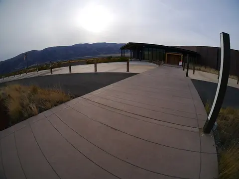 A modern building exterior with a paved walkway and mountains in the background.
