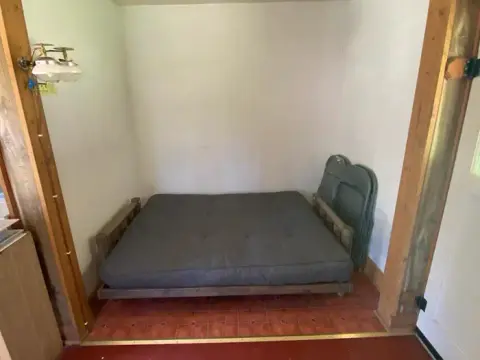 A futon bed inside a room with white walls and red tiled floor.