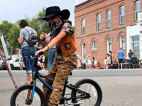 A young person in cowboy costume rides a bicycle outdoors.
