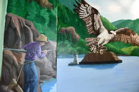 A painted mural showing a person pulling a rope next to a large bird flying over water.