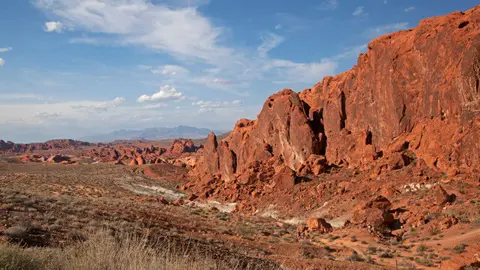 Red rock landscape with sparse desert vegetation under a blue sky with clouds.