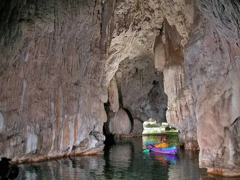 A person kayaking inside a scenic limestone cave with water.