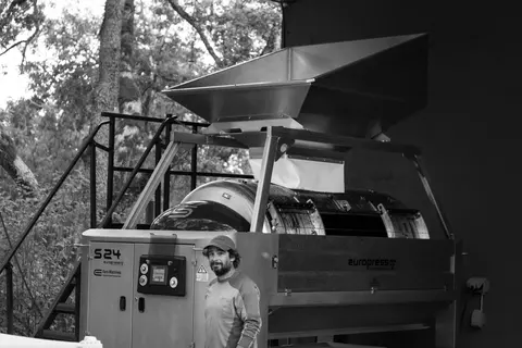 A man stands next to a large industrial press machine outdoors.