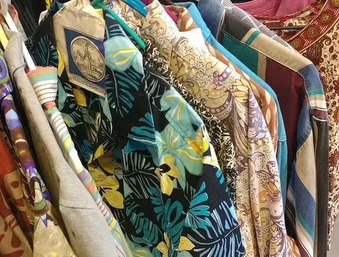 A rack of colorful patterned shirts hangs closely together.