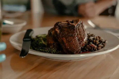 A plate of cooked meat, rice, and broccoli on a wooden table.