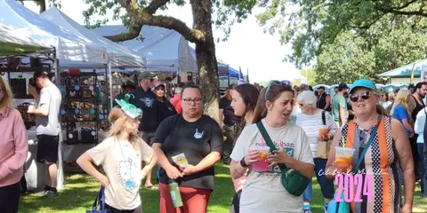 A crowd of people enjoying an outdoor market event with white tents.