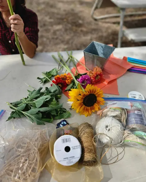 A person prepares flowers and crafting supplies on a table.