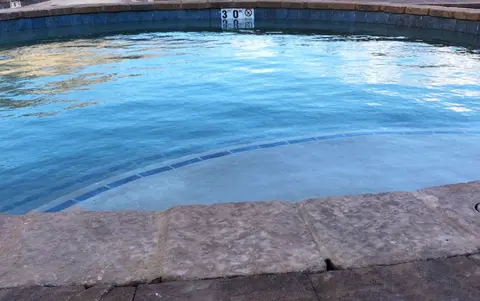 A view of a stone-bordered swimming pool with water.
