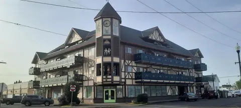 A multi-story building featuring alpine-style architecture and a clock tower is viewed from the street.