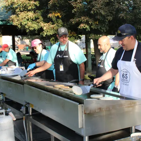 People cook pancakes on large outdoor griddles.