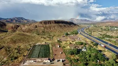 An aerial view shows a farm and a nearby highway in a mountainous landscape.