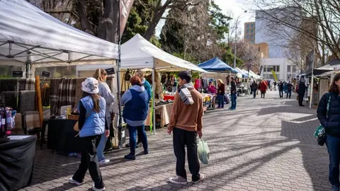A row of outdoor market stalls with white canopies set up along a paved walkway.