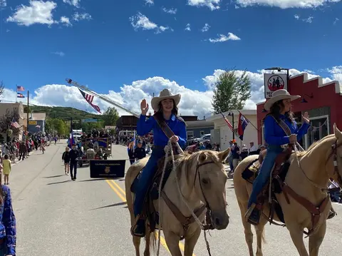 Two people on horseback wave to the crowd during a street parade.
