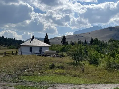 A small white building sits in a grassy landscape with mountains in the background under a cloudy sky.