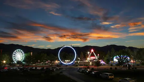 A carnival at dusk with illuminated rides and a colorful sunset over mountains.