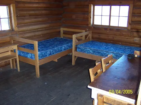An interior view of a log cabin bedroom with two twin beds and a table.