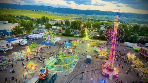 An elevated view of a brightly lit carnival at dusk with rides and people.