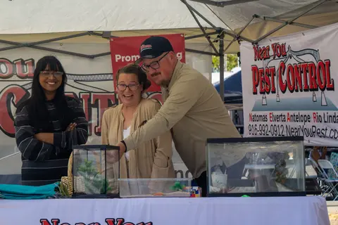 Three people stand behind a booth table with aquariums and banners.