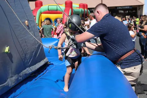 A man assists a young child getting ready for a climbing activity at an outdoor event.