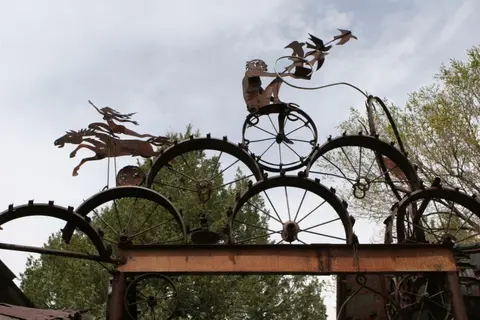 A metal sculpture made of wheels and figures of people and animals against a cloudy sky.