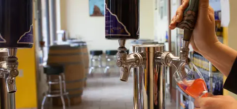 A person pours a beverage from a tap into a glass.