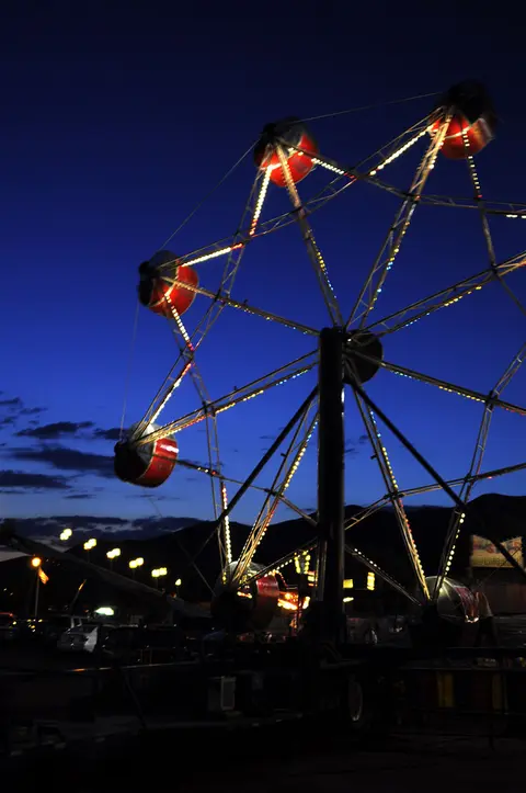 A brightly lit Ferris wheel stands against a dark blue evening sky.