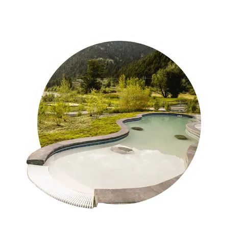 An outdoor swimming pool set in a natural landscape with mountains in the background.