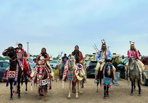 Several people in traditional regalia sitting on horses outdoors.