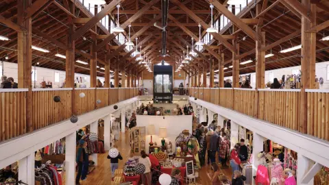 People shop at an indoor market in a large historic wooden building.
