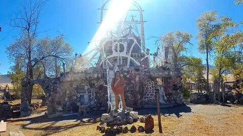 A stone and concrete folk art structure outdoors under a bright sunny sky.
