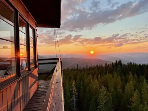 A view of the sunset from a fire lookout tower overlooking a forested mountain range.
