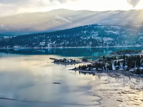 A scenic view of a lake surrounded by snow-dusted mountains and forests.