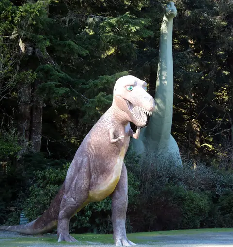 A photo of dinosaur statues set in a wooded area.