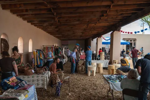 People browsing stalls at an outdoor craft market under a wooden porch.