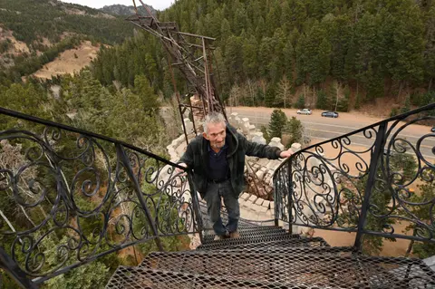 A man climbs a metal spiral staircase overlooking a forested hillside.