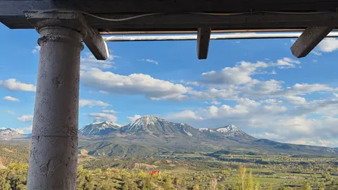 A view of snow-capped mountains and a valley from under a porch roof.