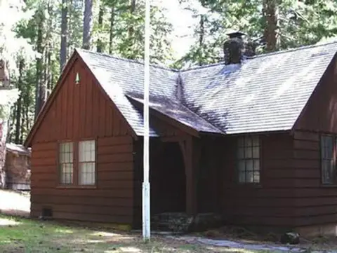 A brown wooden cabin stands surrounded by trees.