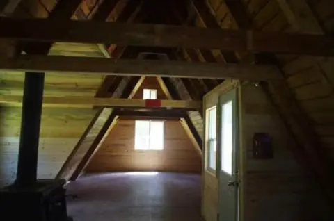 An interior view of a wooden A-frame structure with exposed beams and a window at the end.