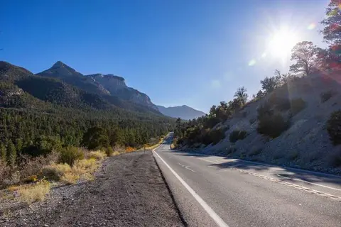 A scenic road winds through a mountainous landscape under a bright sunny sky.