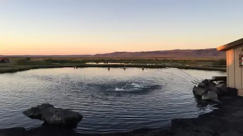 A hot spring pool at sunset with hills in the background.